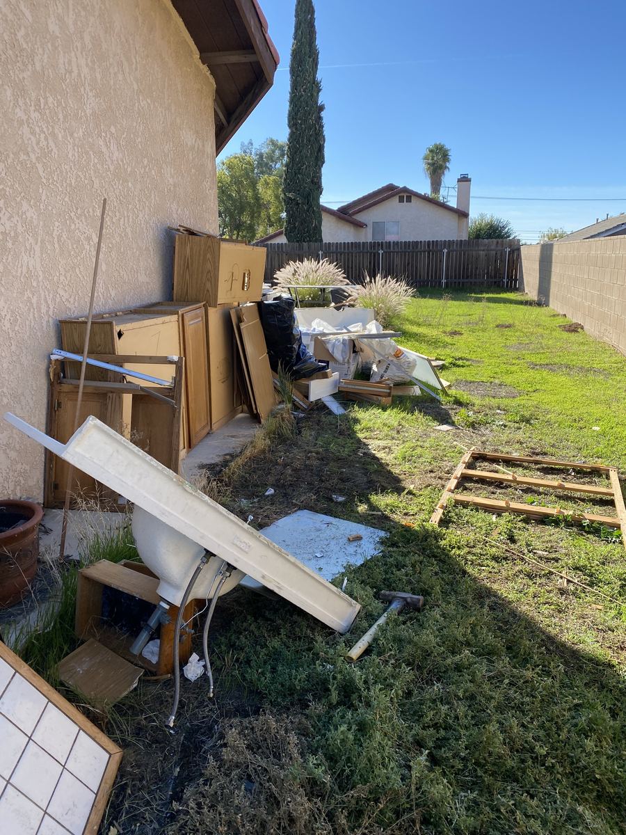 Pile of old cabinets, vanity and tile along the side of a house